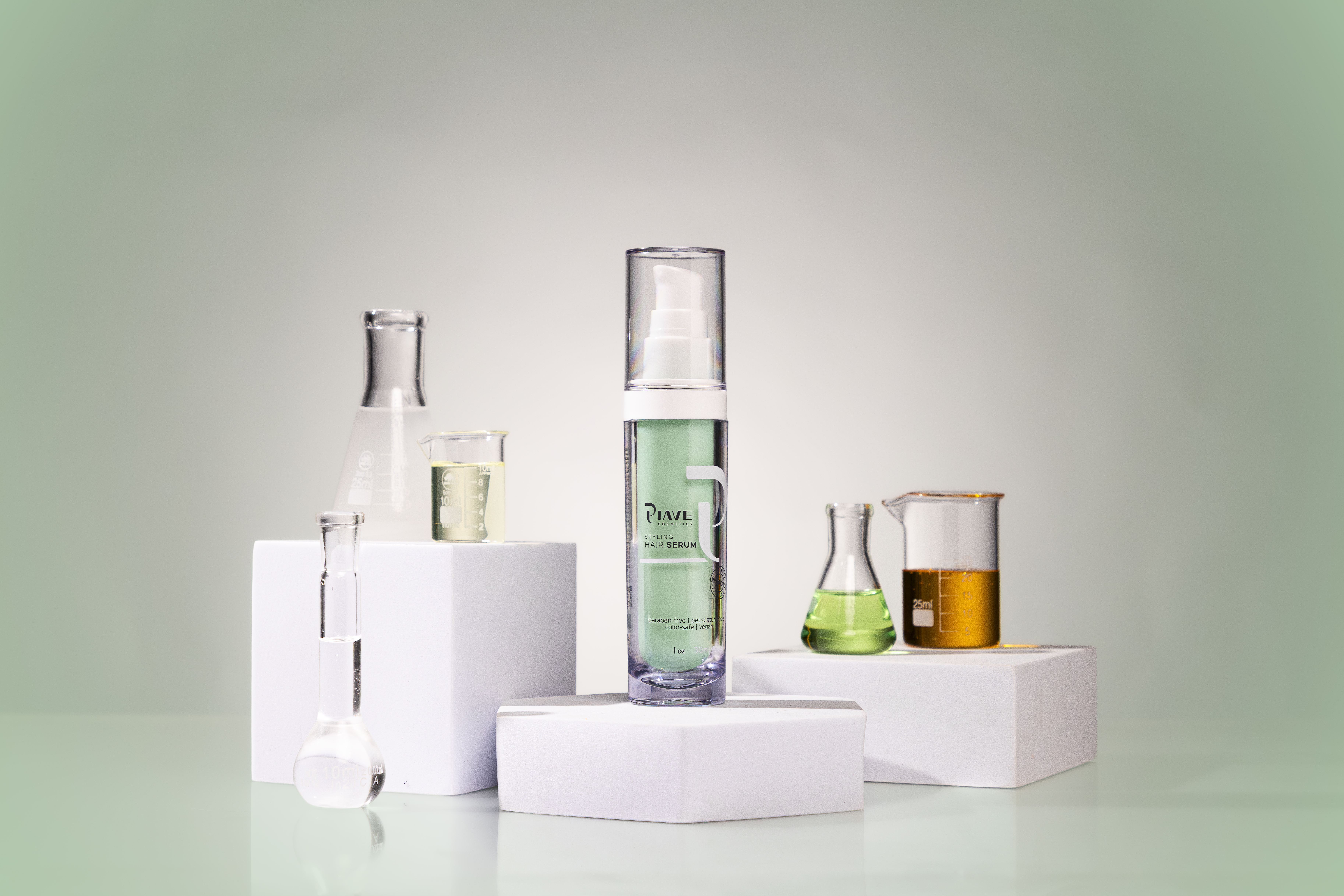 Frasco transparente de sérum capilar Piave com líquido verde, posicionado ao centro sobre blocos brancos, rodeado por vidrarias de laboratório como béqueres e erlenmeyers com líquidos coloridos em verde, amarelo e dourado